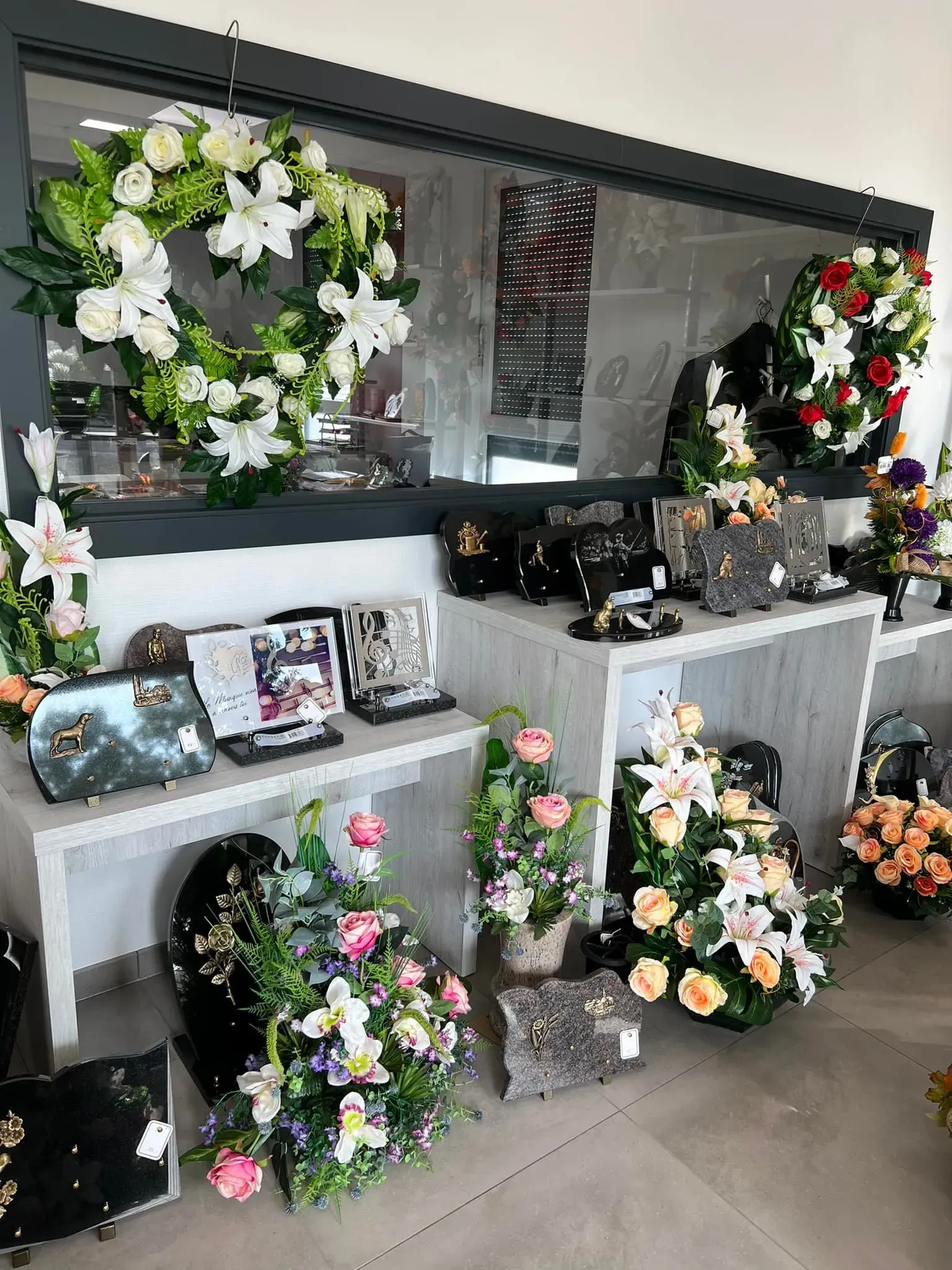 Couronnes de fleurs et plaques commémoratives exposées en magasin.